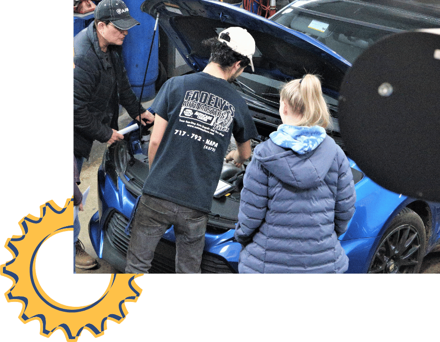 Technician explaining engine repairs to customers under open hood at Fadely’s Auto Masters.