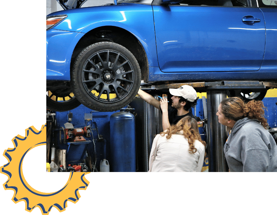 Technician inspecting blue vehicle on lift with customers observing.