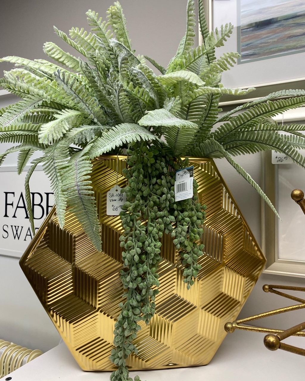 Green faux fern in a gold geometric pot on a store display table