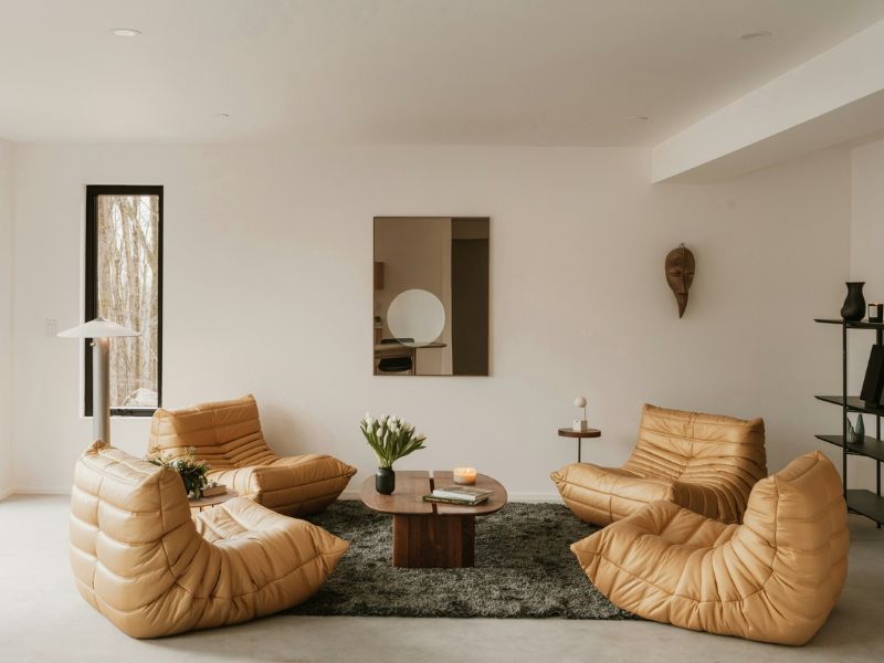 Modern living room with tan lounge chairs, low table, rug, wall mirror, and minimalist decor