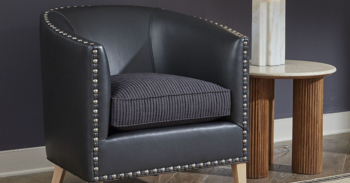 Black upholstered armchair with nailhead trim beside a small round side table