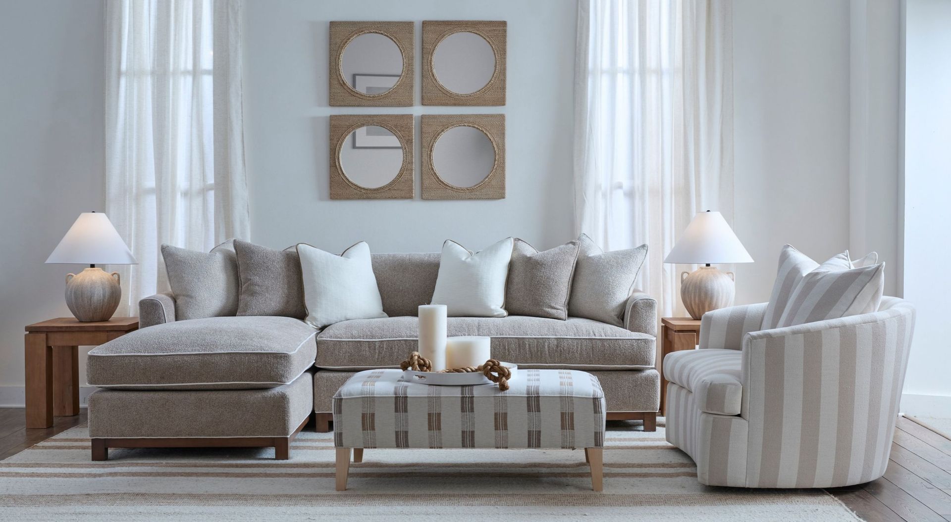 Bright neutral living room with a sectional sofa, striped chairs, coffee table, lamps, and wall art by a window