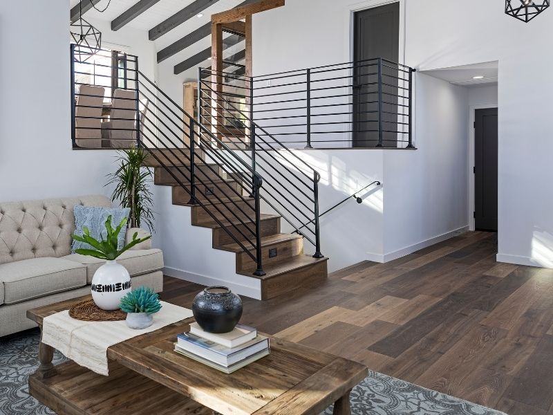 Modern living room with floating staircase, wood floors, and tufted sofa beside a coffee table