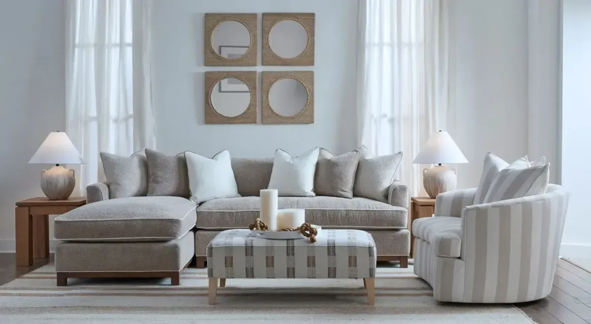 Bright neutral living room with beige sectional sofa, striped chair, ottoman, lamps, and wall art