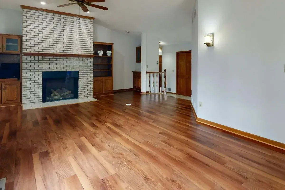 Empty living room with hardwood floors, white walls, a brick fireplace, and a ceiling fan.