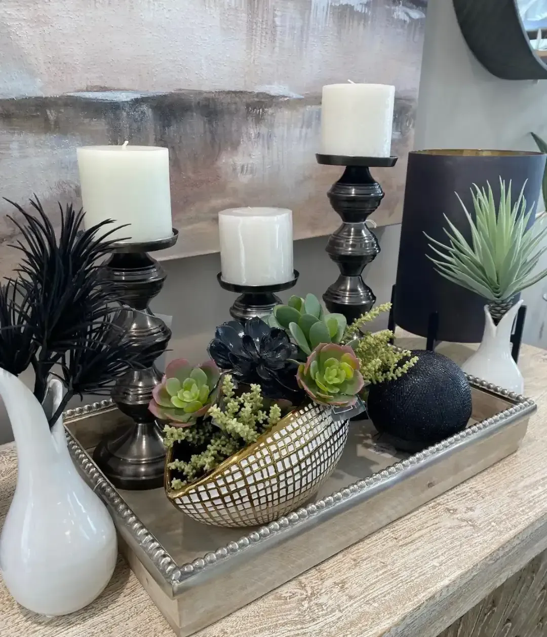 Decorative tray with white candles, black and white vases, and small succulents on a table