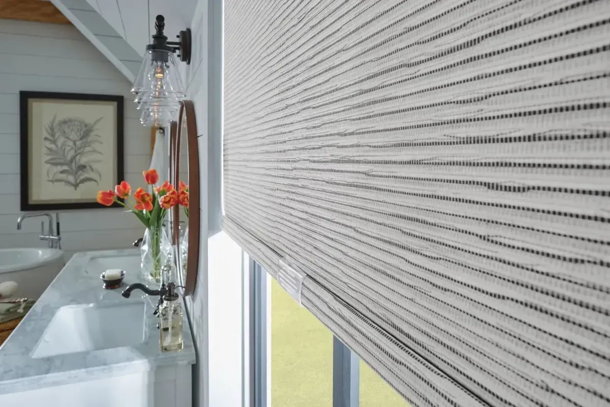 White horizontal window blinds with sunlight filtering through, above a white windowsill trim