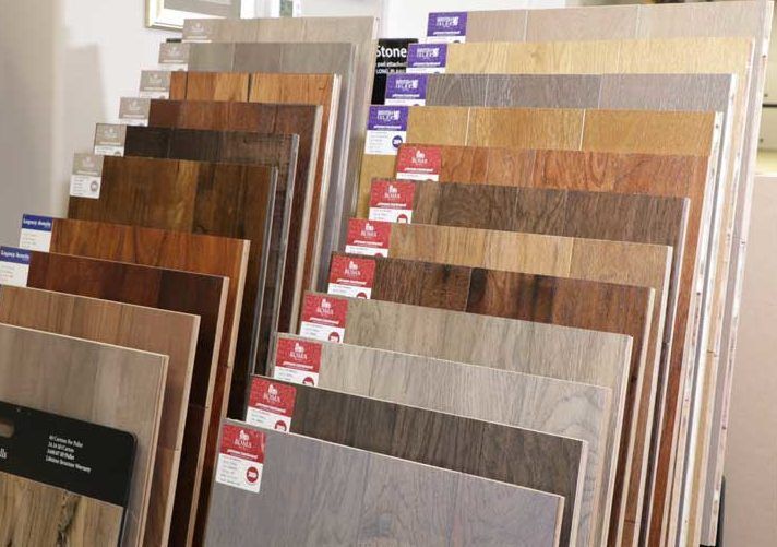 Display of wood flooring samples in various colors and finishes, arranged on racks.