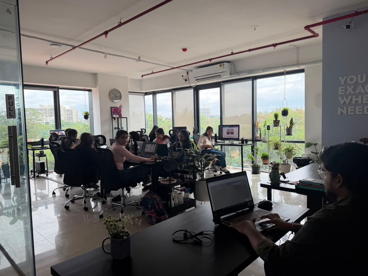 People seated around laptops in a bright glass-walled meeting room with large windows.