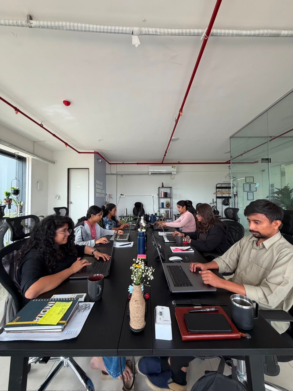 People working at laptops around a long conference table in a bright office meeting room.