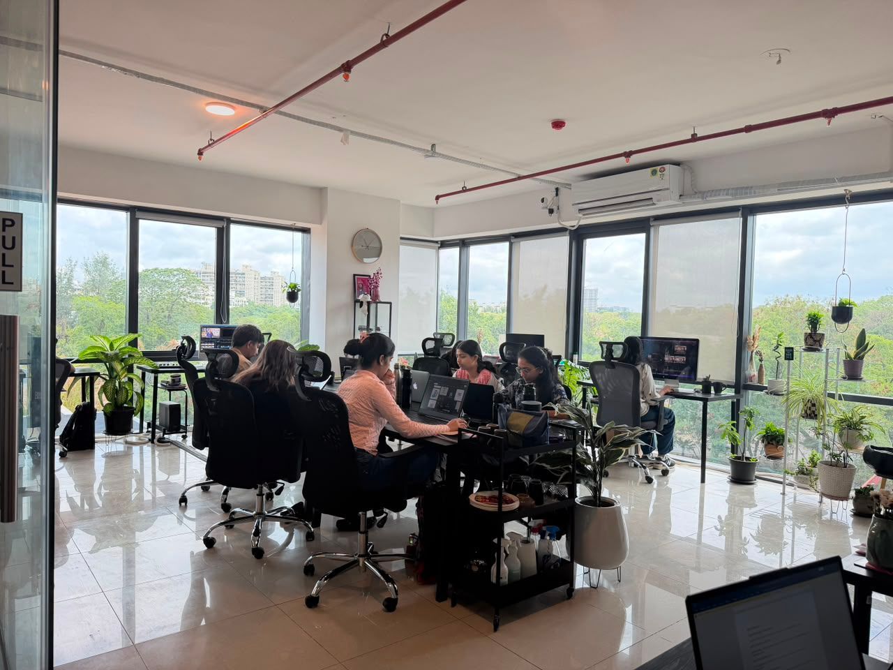 People working in a bright open office with desks, computers, and large windows.