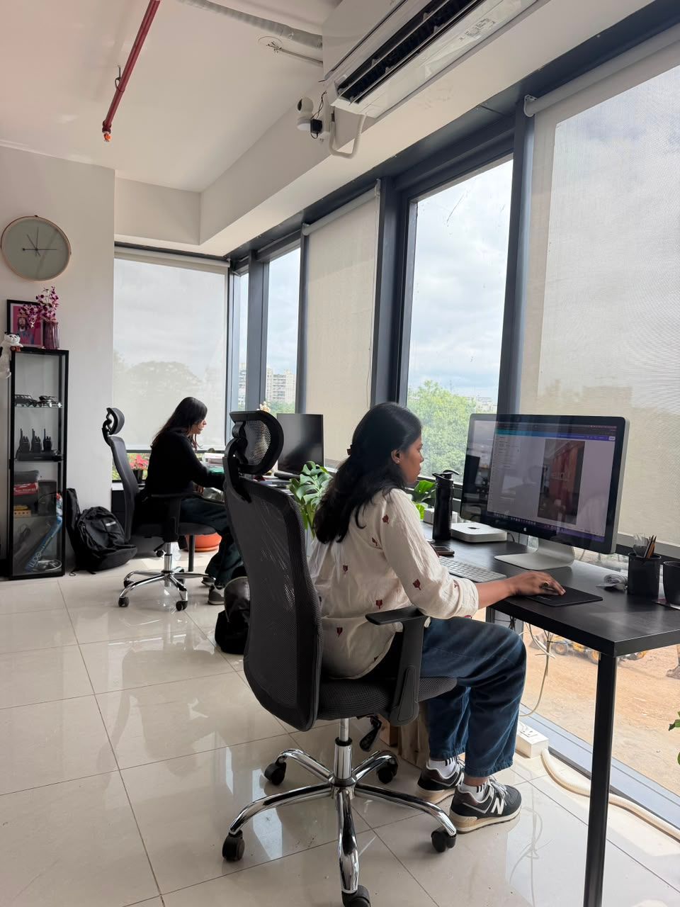 Two people working at computers in a bright office with large windows and city views