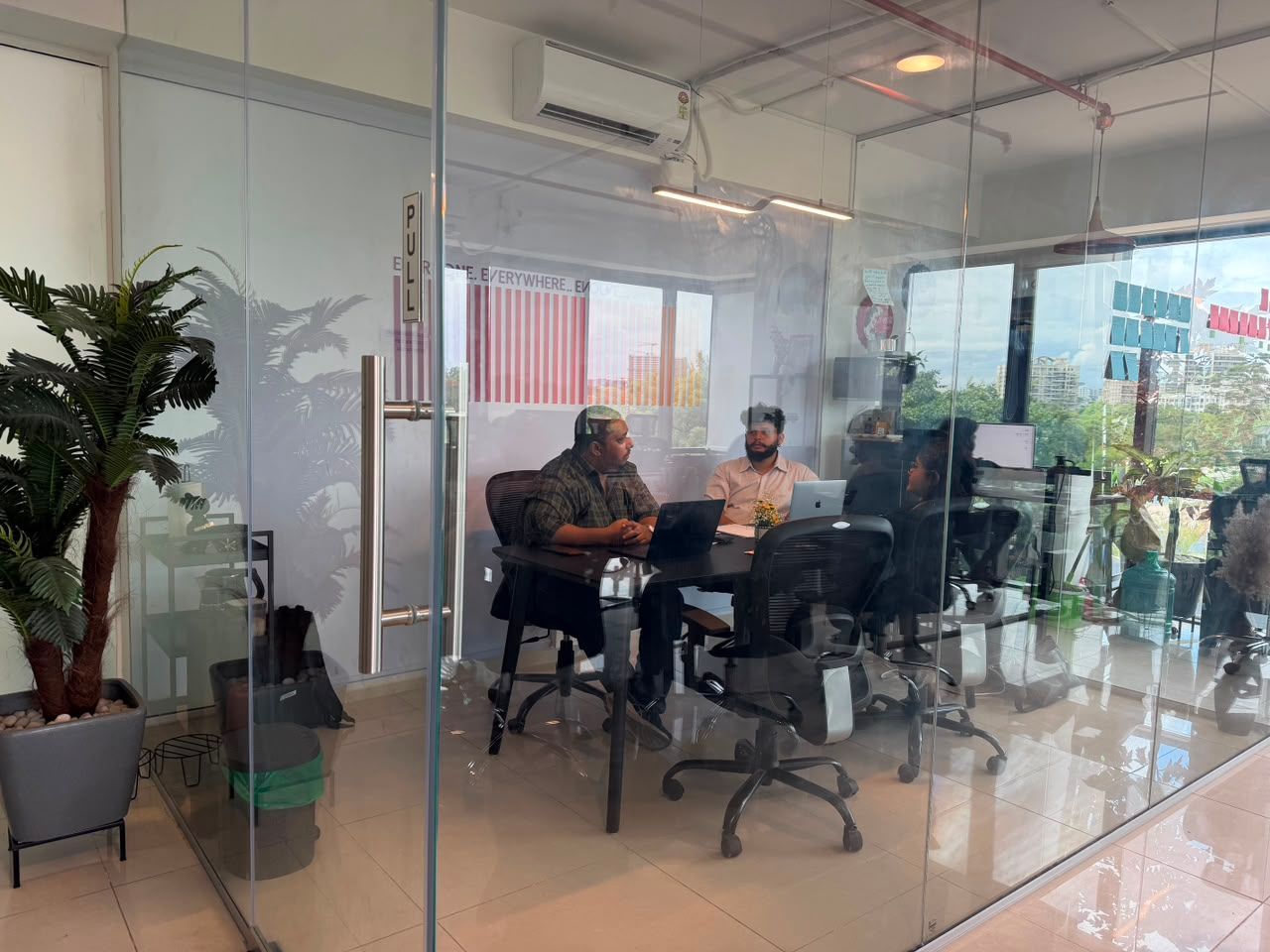 People seated at a glass-walled conference table in a bright office meeting room