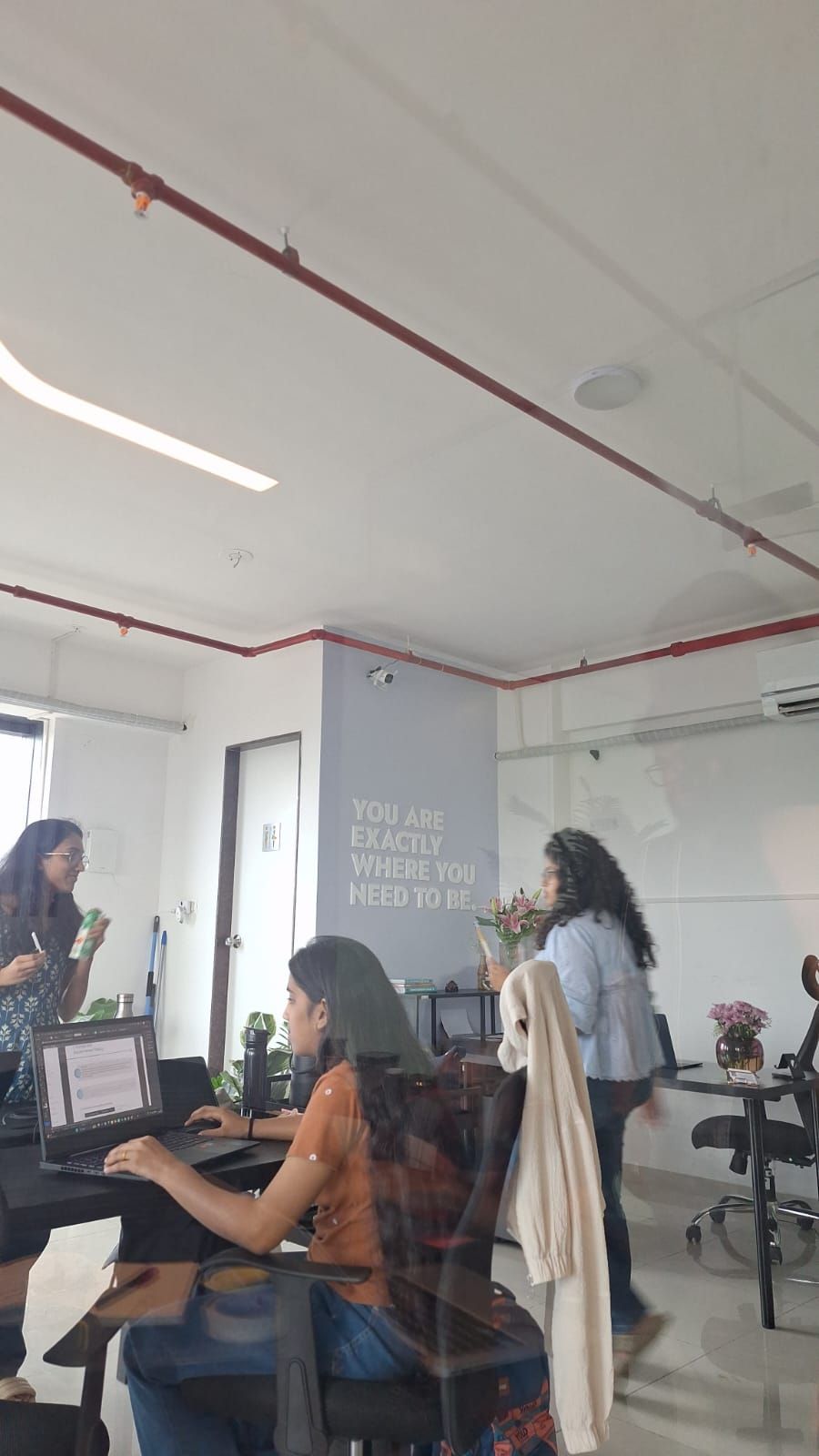 Small office with people working at desks and a whiteboard on the wall.