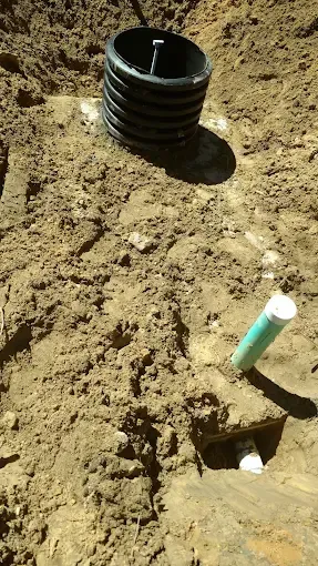 Open dirt trench with black corrugated pipe and a green pipe sticking out nearby
