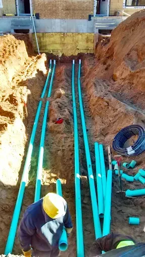 Worker laying blue pipes in a narrow trench at a construction site