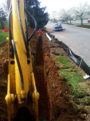 Yellow excavator digging a trench beside a road with workers and traffic in the background