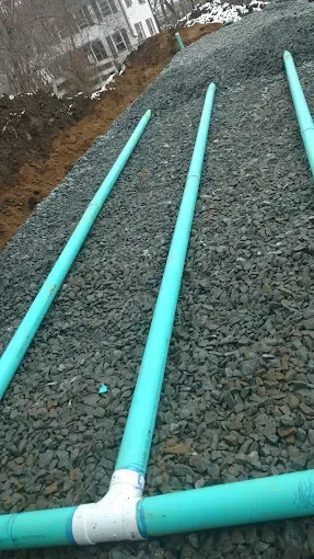 Turquoise pipes laid across a gravel slope beside a fence and snow patches