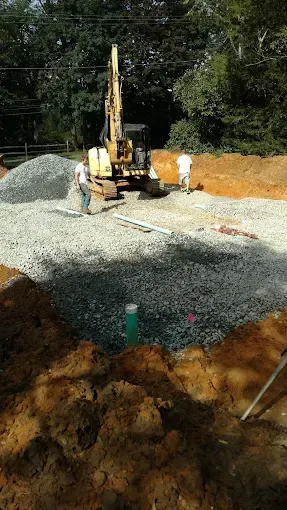 Small excavator on a gravel construction site with dirt piles and trees in the background
