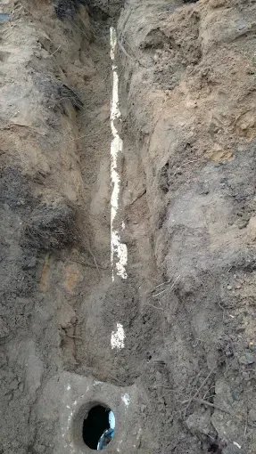 Vertical dirt trench with a small pipe opening at the bottom and a bright crack of light running up the center