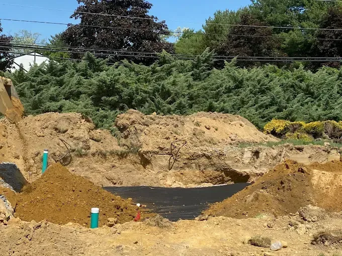 Construction site with sandy dirt mounds, black tarp, and green trees in the background