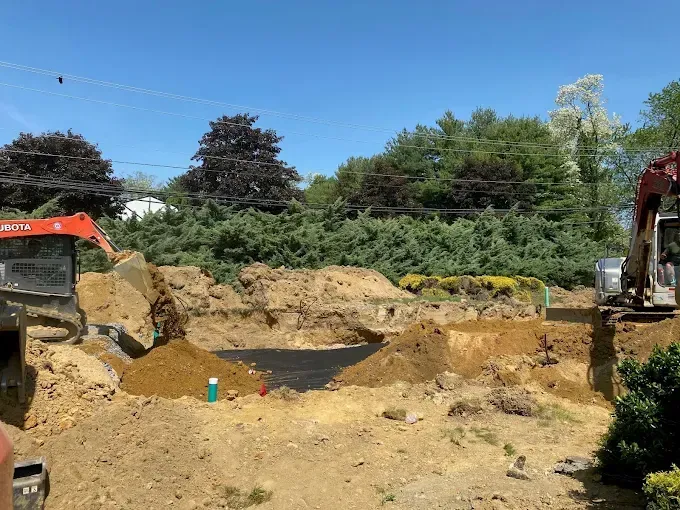 Excavation site with two excavators digging a large dirt pit under a blue sky.