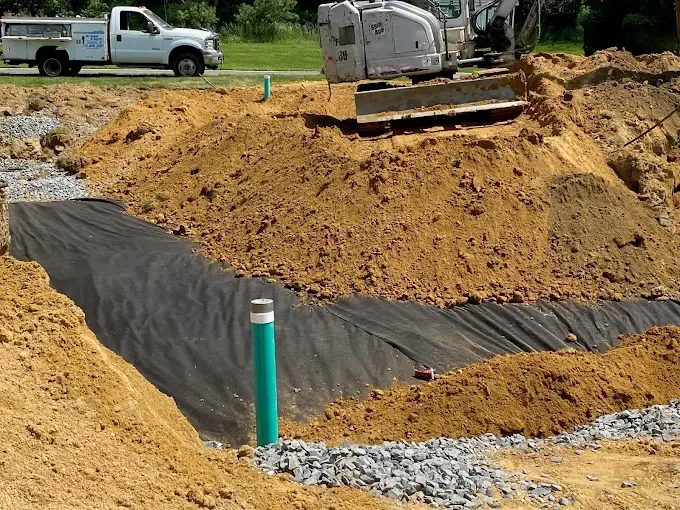 Construction site with excavator shaping a dirt trench, black geotextile lining, and a white truck nearby
