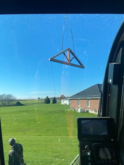 A crane is lifting a wooden triangle in a field.