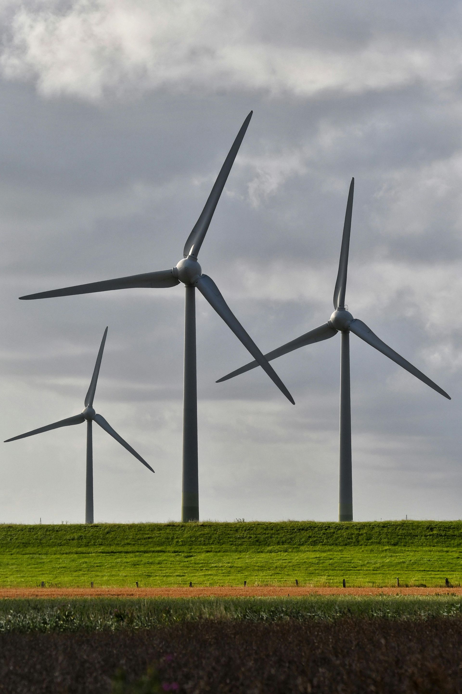 Three wind turbines on a grassy field under a cloudy sky