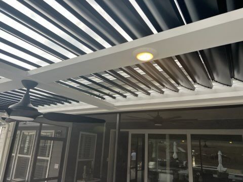 Covered patio with black-and-white striped pergola, ceiling lights, and sliding glass doors at a house
