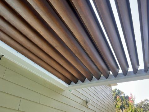 Pergola with wooden slats and bright skylight above a house exterior wall