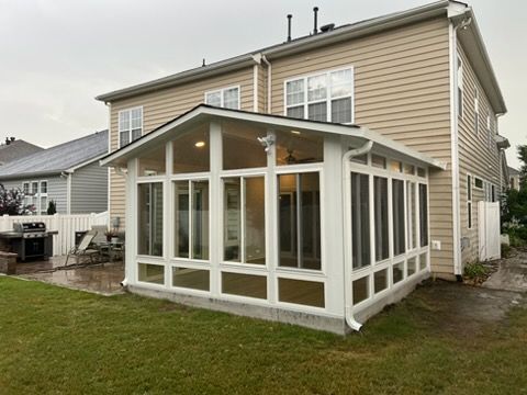 White sunroom addition with large windows and sloped roof on the back of a beige house in a grassy yard