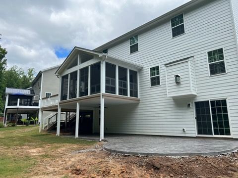 White two-story house with screened porch and deck over a concrete patio, viewed from the backyard