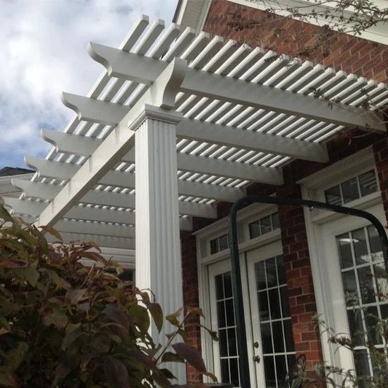 White pergola over a brick house patio with French doors and a flowering shrub