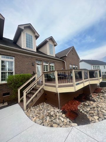 Brick house with raised wooden deck, stairs, and stone landscaping in a suburban yard.