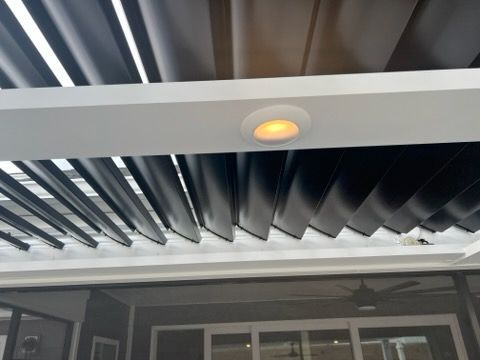 Close-up of a black slatted awning with a lit recessed ceiling light above glass doors