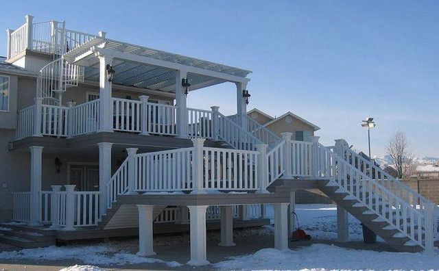 Snowy house with white wraparound porch and stairs under a clear blue sky