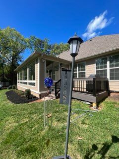 Single-story house with screened porch, lamp post, and lawn under a blue sky