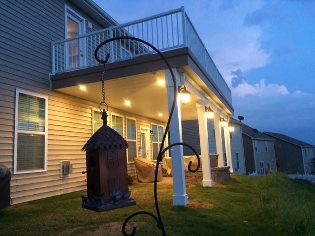 Lit porch at dusk with hanging bird feeder beside a two-story house and grassy yard