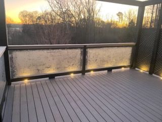 Empty screened-in deck with gray flooring and warm lights at sunset.