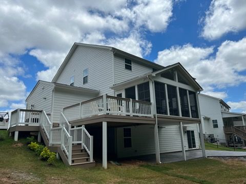 White house with a raised deck, stairs, and screened porch under a partly cloudy sky