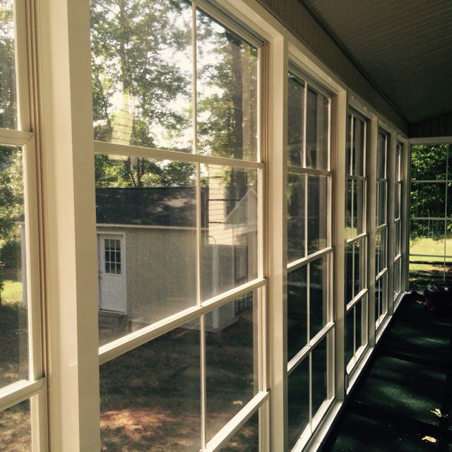 Sunlit screened porch with white-framed windows overlooking a backyard and shed