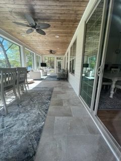 Covered outdoor patio with tiled floor, dining table, ceiling fan, and sliding glass doors beside a pool area