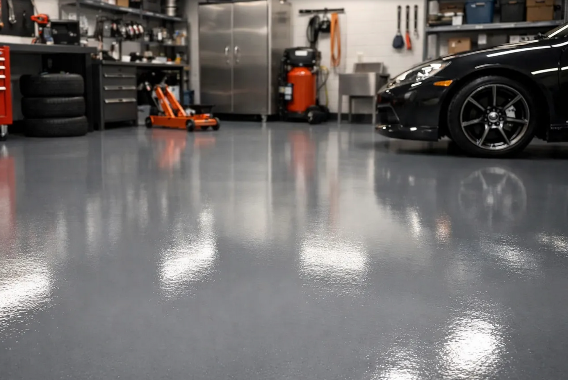 Glossy garage floor with a black sports car, tools, shelves, and an orange floor jack in the background
