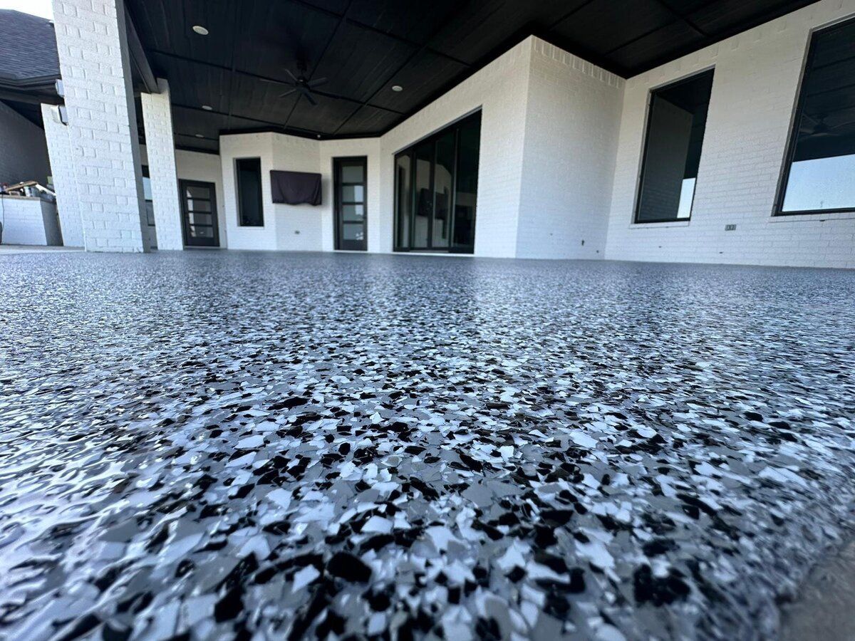Close-up of a speckled, gray epoxy floor on a patio, with a modern white building in the background.