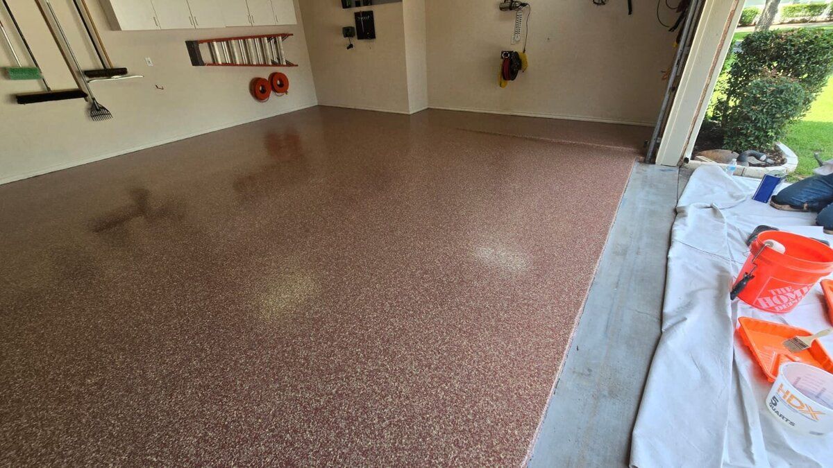 Garage floor with brown speckled epoxy coating. Tools and garage door are visible.