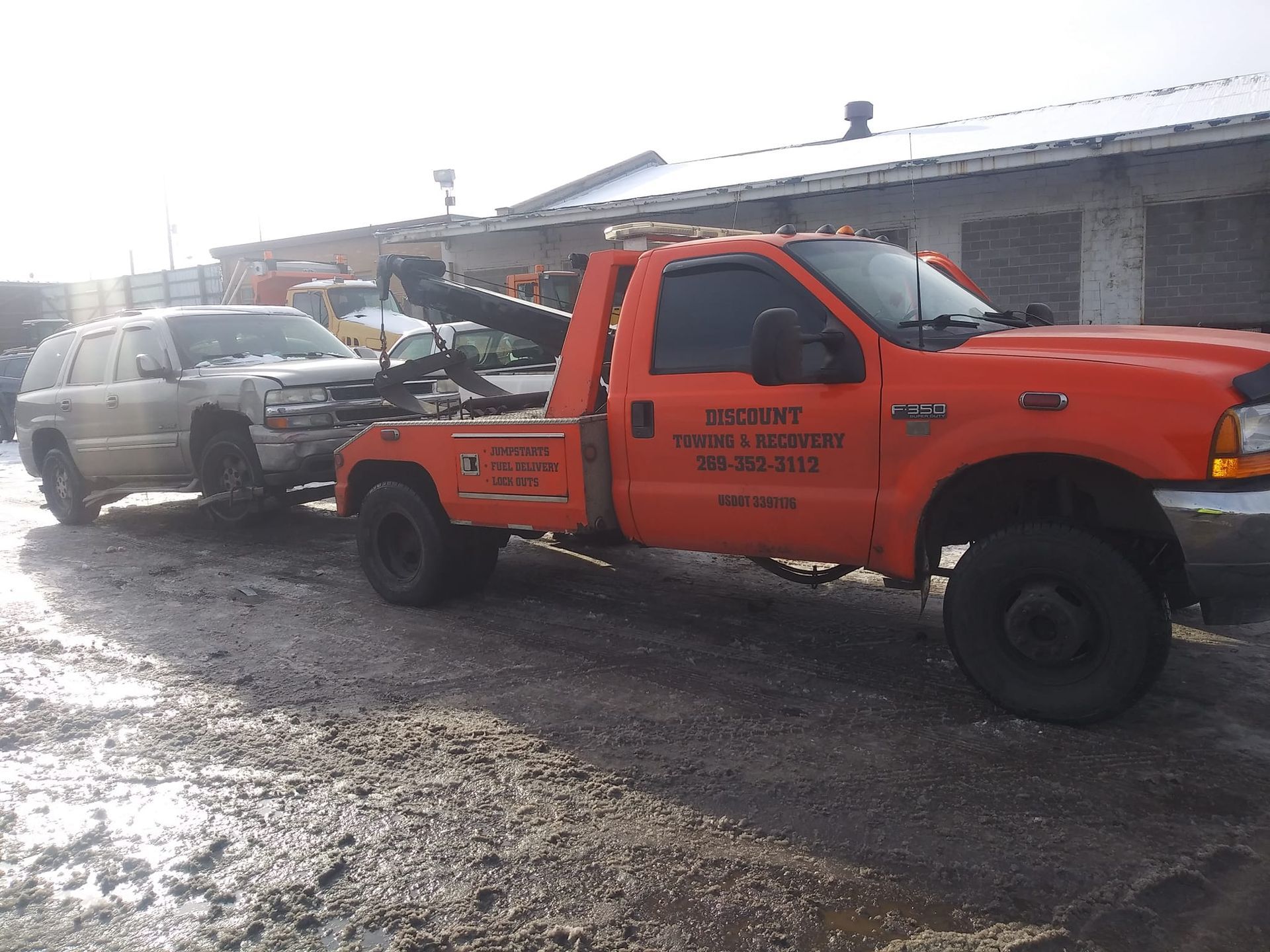 An orange tow truck is carrying a white suv