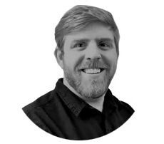 A man with a beard is smiling in a black and white photo.