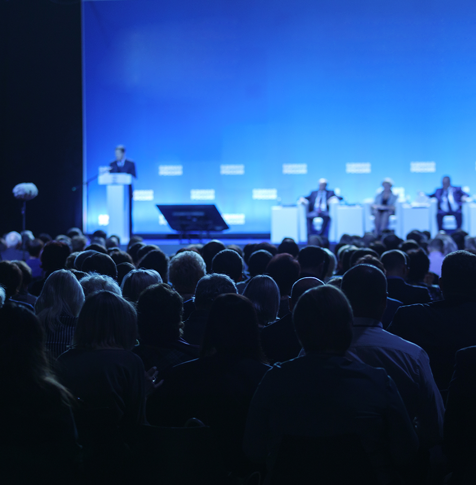 A crowd of people are sitting in front of a stage with a blue background