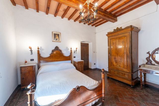 Camera da letto rustica con letto in legno intagliato, armadio, cassettiera e soffitto con travi a vista.